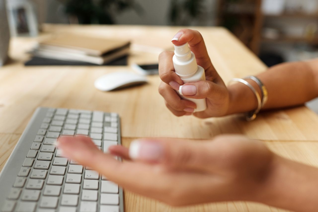 Personne se désinfectant les mains à un bureau avec un vaporisateur, un clavier et une souris d'ordinateur.